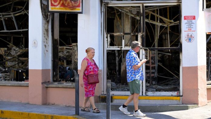 1771977834_tourists-walk-past-a-burned-shop.jpg